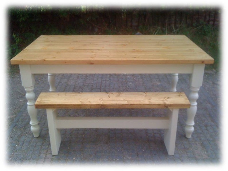 May include: A white farmhouse style table with a natural wood top and a matching bench. The table has turned legs and the bench has a simple design.