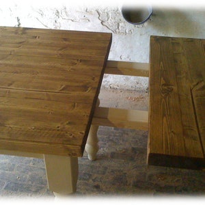 May include: A wooden table with a brown top and white legs. The table has a leaf that can be extended to make it longer.