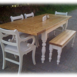 May include: A white farmhouse style dining table with a natural wood top and turned legs. The table is set with four chairs and a bench. The chairs and bench are painted white with a distressed finish.
