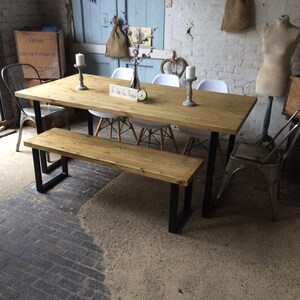May include: A rustic wooden dining table with black metal legs and a matching bench. The table is set with white chairs and a centrepiece of flowers and candles.