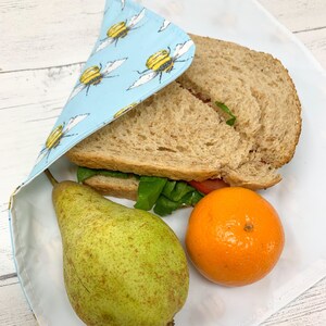 Op de afbeelding: Een herbruikbare voedselverpakking in blauw en geel met een bijenpatroon, met daarin een sandwich, een peer en een mandarijn.