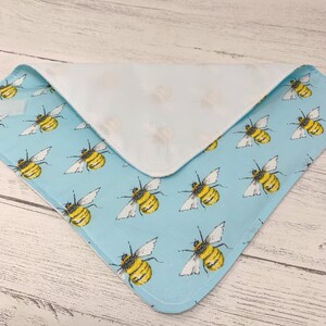 Op de afbeelding: Een lichtblauwe stoffen slab met een witte achterkant en een herhalend patroon van gele en zwarte bijen.
