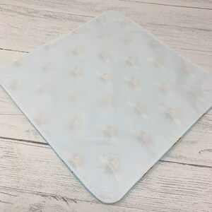 Op de afbeelding: Een lichtblauwe baby spuugdoek met een wit en geel bijenpatroon. De doek heeft een vastgenaaide flap aan de ene kant.