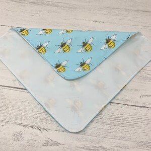 Op de afbeelding: Een lichtblauwe bandana met een witte rand en een patroon van gele en zwarte bijen. De bandana is dubbelgevouwen en het patroon is aan beide kanten zichtbaar.