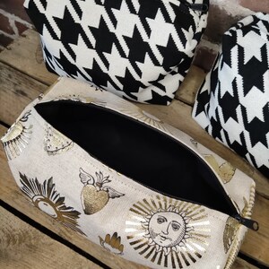 May include: A beige zippered pouch with a gold foil design of suns, hearts, and wings. The pouch is open and the inside is black.