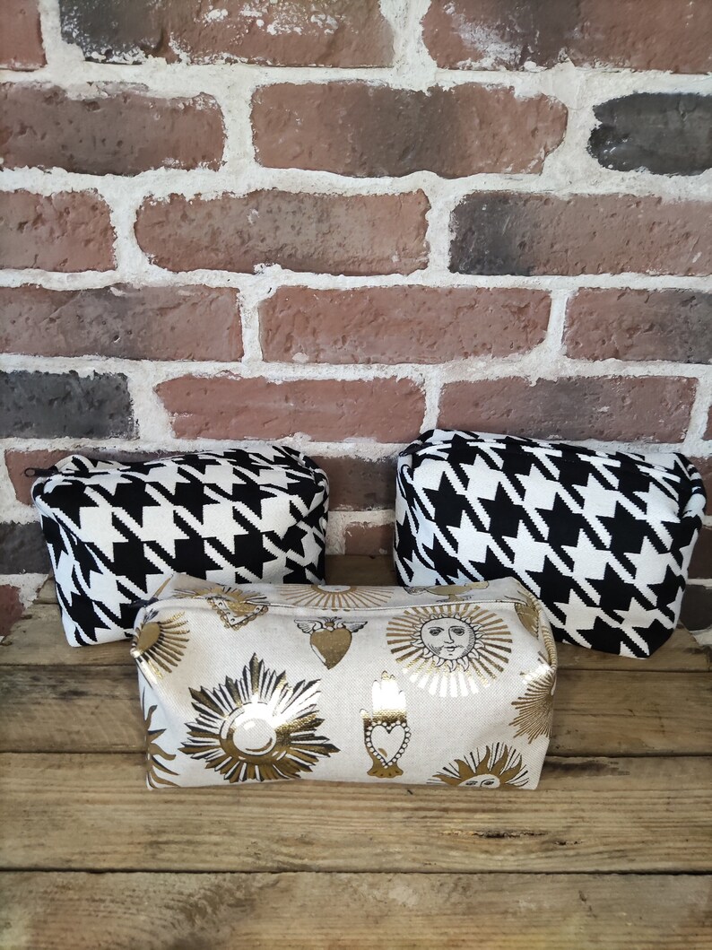 May include: Three cosmetic bags. Two are black and white houndstooth fabric. One is beige with gold metallic sun and heart designs.
