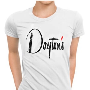 Może przedstawiać: Biała koszulka z napisem "Dayton's" w czarnym skrypcie. Apostrof jest czerwony. Koszulka ma okrągły dekolt i krótkie rękawy. Materiał wydaje się miękki i wygodny.
