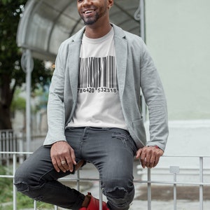 May include: White t-shirt with a black barcode design and the numbers 786420 532318. The person is wearing a gray blazer, black distressed jeans, and red sneakers.