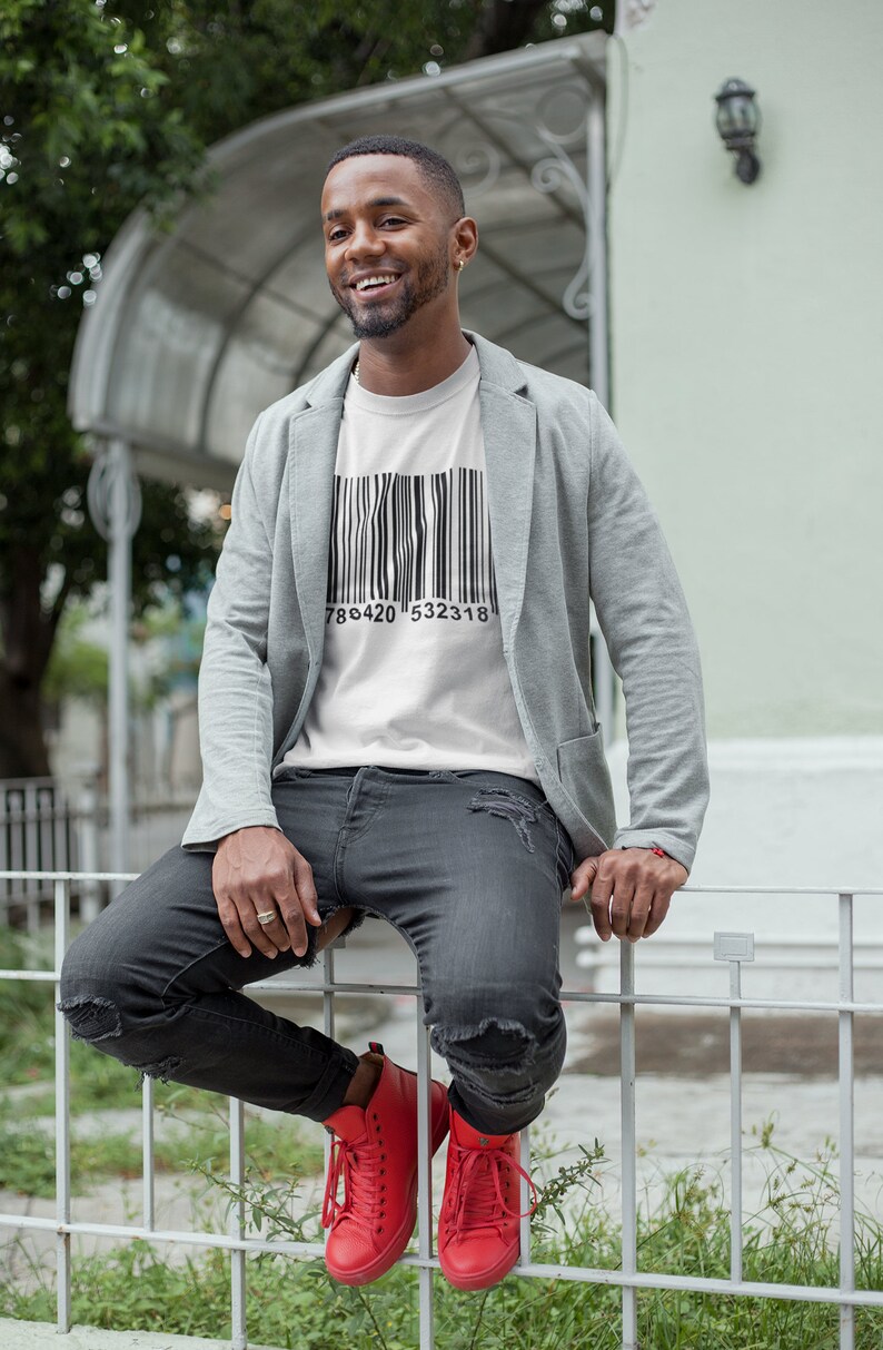 May include: White t-shirt with a black barcode design and the numbers 786420 532318. The person is wearing a gray blazer, black distressed jeans, and red sneakers.
