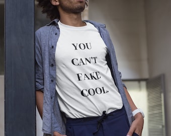 May include: A white t-shirt with the text "YOU CAN'T FAKE COOL." printed in black. The person wearing the shirt is standing in front of a wall.