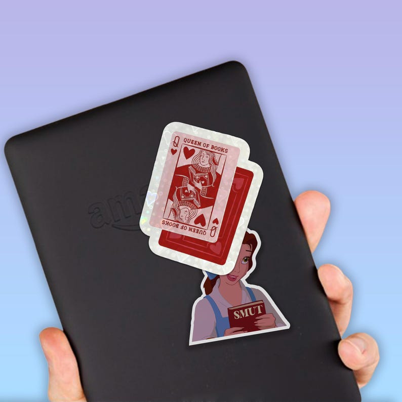 May include: A black e-reader with stickers of a playing card, a cartoon woman, and a book. The playing card is a Queen of Books with a red background. The cartoon woman is holding a book with the word "SMUT" on it.