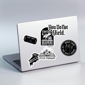 Puede incluir: Un port&aacute;til con varias pegatinas en blanco y negro. Las pegatinas presentan texto y gr&aacute;ficos, incluyendo "You Do Not Fantasy Yield", "Readers Book Club", "Night Court", "Rhysand" y "City of Starlight".