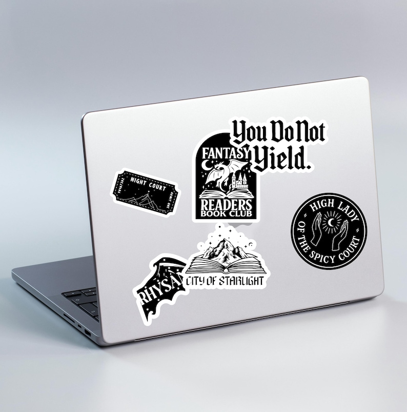 Puede incluir: Un port&aacute;til con varias pegatinas en blanco y negro. Las pegatinas presentan texto y gr&aacute;ficos, incluyendo "You Do Not Fantasy Yield", "Readers Book Club", "Night Court", "Rhysand" y "City of Starlight".