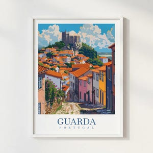 May include: A framed art print depicting Guarda, Portugal. The illustration shows a European town with a castle on a hill, surrounded by buildings with orange roofs and colourful facades. The text "GUARDA PORTUGAL" is displayed at the bottom of the print.