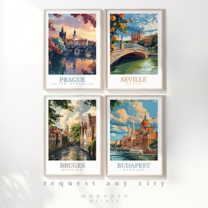 May include: Four framed travel art prints showcasing cityscapes of Prague, Seville, Bruges, and Budapest. Each print has a white border and includes the city name and country. The prints are in a vertical orientation and are displayed against a white background.