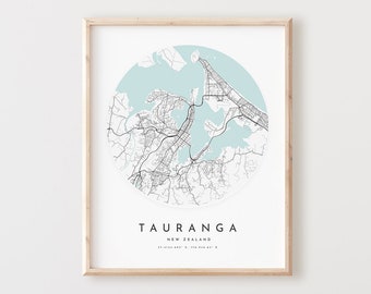 May include: A black and white map of Tauranga, New Zealand, in a light blue circle on a white background. The map is framed in a light wood frame.