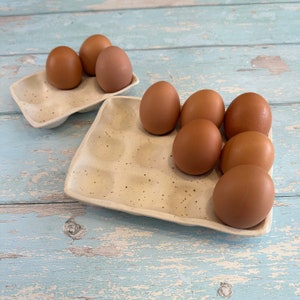 Op de afbeelding: Twee witte keramische eierdozen met bruine eieren. De ene doos heeft vier eieren en de andere zes eieren.