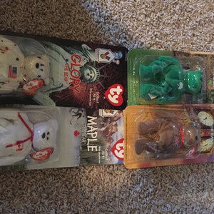 May include: Five Ty Beanie Babies, each representing a different country. The bears are in their original packaging, with the country's flag and landmarks on the back. The bears are: Britannia, Erin, Maple, Glory, and a white bear with a Canadian flag.