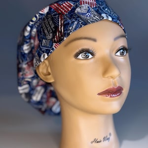 May include: A blue and red patterned surgical scrub hat with a variety of military-themed designs, including American flags, military insignia, and the words "Honor, Respect, Integrity, and Service".