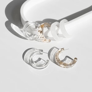 May include: A pair of clear hoop earrings with gold flecks. One pair is solid clear, the other has gold flecks throughout.