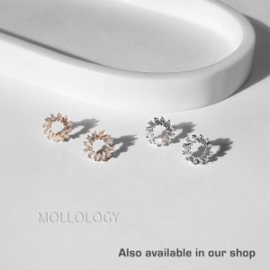 May include: Three pairs of small, round, hoop earrings with a circle of small, clear, baguette-shaped stones. The earrings are shown on a white surface. The earrings are available in gold, silver, and rose gold.