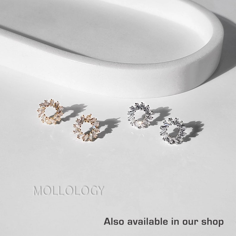 May include: Three pairs of small, round, hoop earrings with a circle of small, clear, baguette-shaped stones. The earrings are shown on a white surface. The earrings are available in gold, silver, and rose gold.