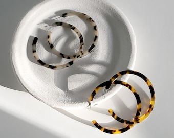 May include: Two pairs of hoop earrings, one pair is black and brown tortoise shell, the other is white and brown tortoise shell.