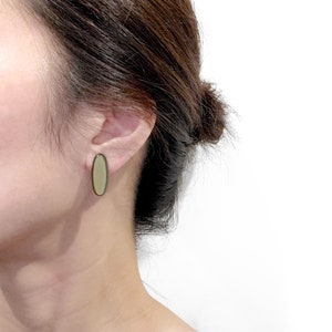 May include: A pair of oval-shaped earrings with a light green and dark green colour scheme. The earrings are made of a smooth, polished material.