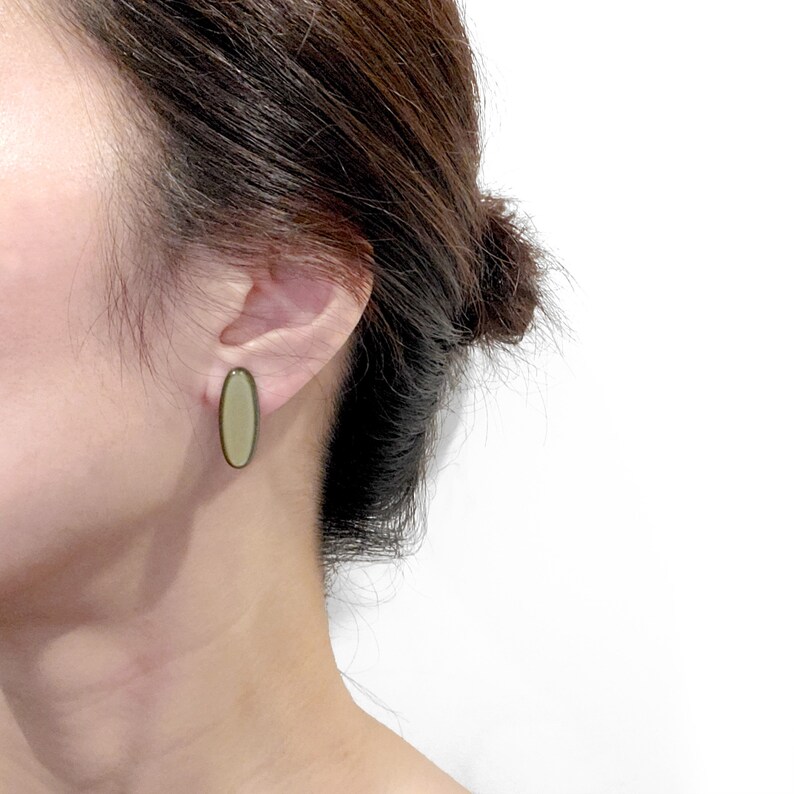 May include: A pair of oval-shaped earrings with a light green and dark green colour scheme. The earrings are made of a smooth, polished material.
