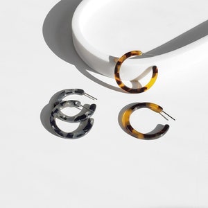 May include: Three pairs of hoop earrings, two are brown and black tortoise shell and one is black and white tortoise shell.