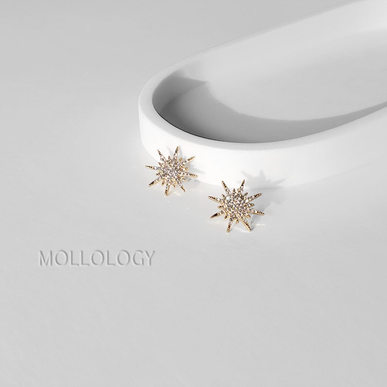 May include: A pair of gold star-shaped earrings with clear crystal accents. The earrings are on a white surface.