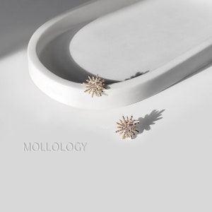 May include: A pair of gold starburst earrings with clear rhinestones. The earrings are on a white surface.