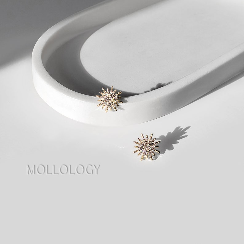 May include: A pair of gold starburst earrings with clear rhinestones. The earrings are on a white surface.