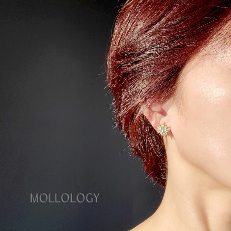 May include: A close-up of a person's ear wearing a gold star-shaped earring with clear crystals.