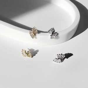 May include: Three pairs of earrings with a fan-shaped design. The earrings are made of silver and gold metal and feature clear cubic zirconia stones.