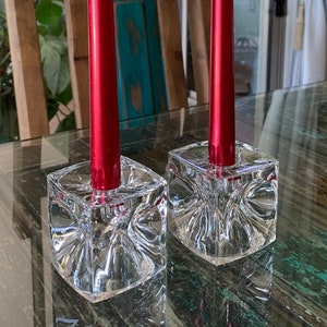 May include: Two red candles in clear glass candle holders with a geometric design.