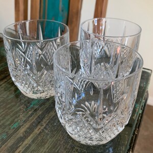 K&ouml;nnte beinhalten: Drei klare Glasbecher mit geschliffenem Glasdesign. Die Gl&auml;ser stehen auf einer Holzoberfl&auml;che.