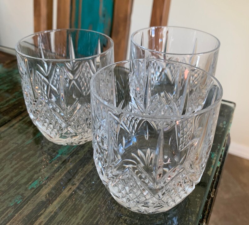 K&ouml;nnte beinhalten: Drei klare Glasbecher mit geschliffenem Glasdesign. Die Gl&auml;ser stehen auf einer Holzoberfl&auml;che.
