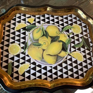 May include: Decorative serving tray with a black and white geometric pattern and a gold-colored rim. The tray features a central image of lemons on a plate, with lemon slices scattered around.
