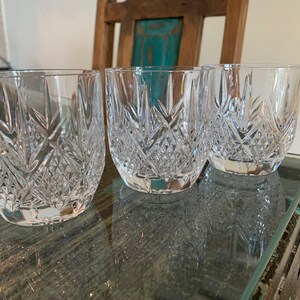 K&ouml;nnte beinhalten: Drei klare Glasbecher mit geschliffenem Kristallmuster. Die Gl&auml;ser stehen auf einem Holztisch mit Glasplatte.
