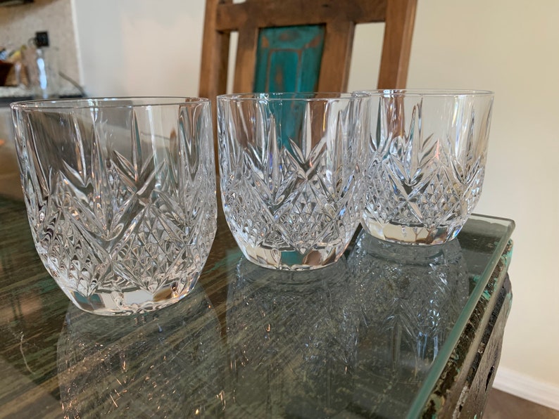 K&ouml;nnte beinhalten: Drei klare Glasbecher mit geschliffenem Kristallmuster. Die Gl&auml;ser stehen auf einem Holztisch mit Glasplatte.