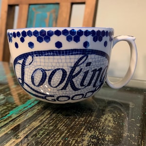 May include: White ceramic mug with a blue and white mosaic design. The mug has a handle and says "Looking Good" in blue lettering.