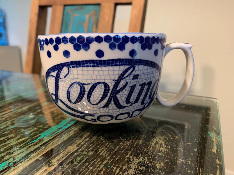 May include: White ceramic mug with a blue and white mosaic design. The mug has a handle and says "Looking Good" in blue lettering.