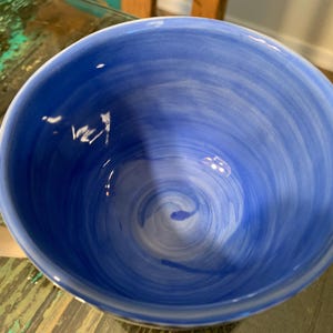 May include: A blue ceramic mug with a white swirl design inside. The mug has a white handle with blue dots.