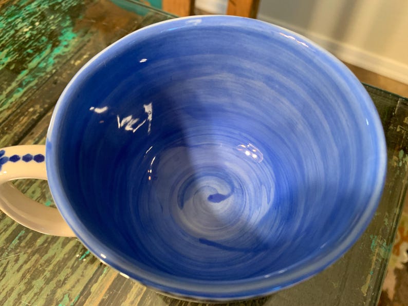 May include: A blue ceramic mug with a white swirl design inside. The mug has a white handle with blue dots.
