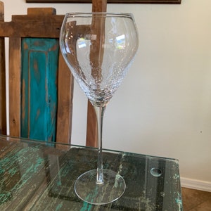 May include: A clear glass wine glass with a textured surface. The glass has a long stem and a wide bowl.