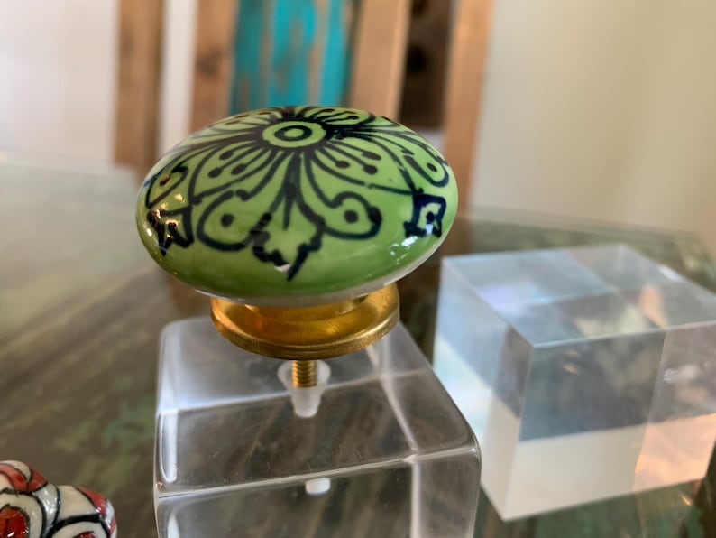 May include: A green ceramic knob with a black and white floral design, mounted on a clear acrylic base.
