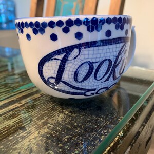 May include: White ceramic mug with a blue and white mosaic design. The mug has a handle and says "Look Good" in a blue mosaic font.