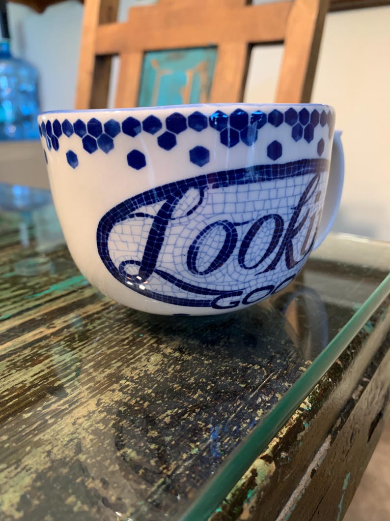 May include: White ceramic mug with a blue and white mosaic design. The mug has a handle and says "Look Good" in a blue mosaic font.