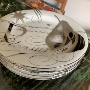 May include: A stack of white ceramic plates with silver trim and decorative script. Each plate features a pear design and a star. The plates are stacked on a glass surface.